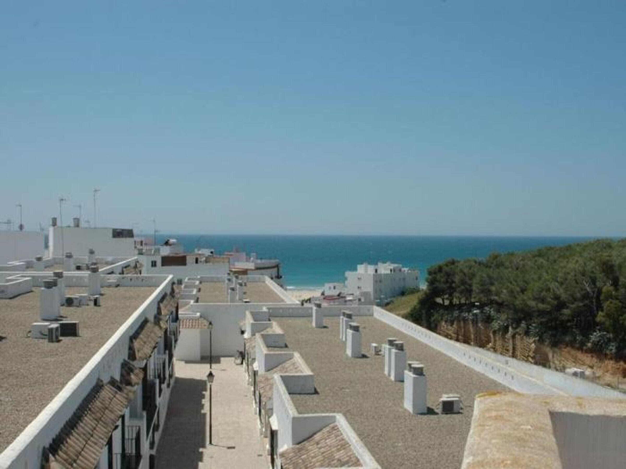 A rooftop terrace with a view of the sea, air conditioning units, and a clear sky.