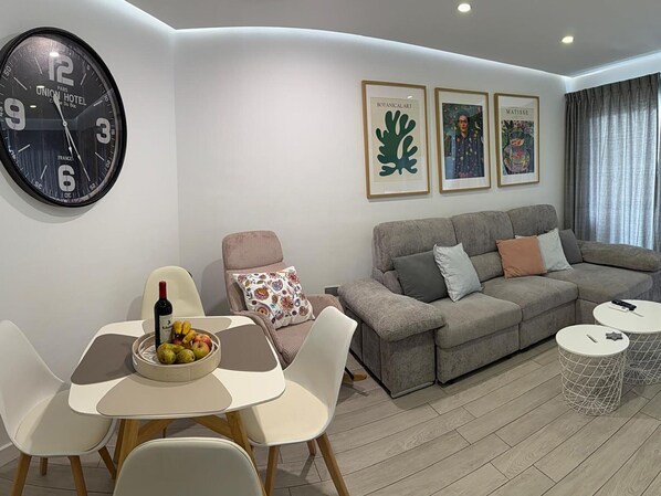 Uma sala de estar moderna com sofá, cadeiras, uma mesa de jantar com frutas, um relógio e obras de arte emolduradas.