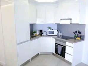 A compact kitchen with white cabinets, a microwave, a stove, and a sink.