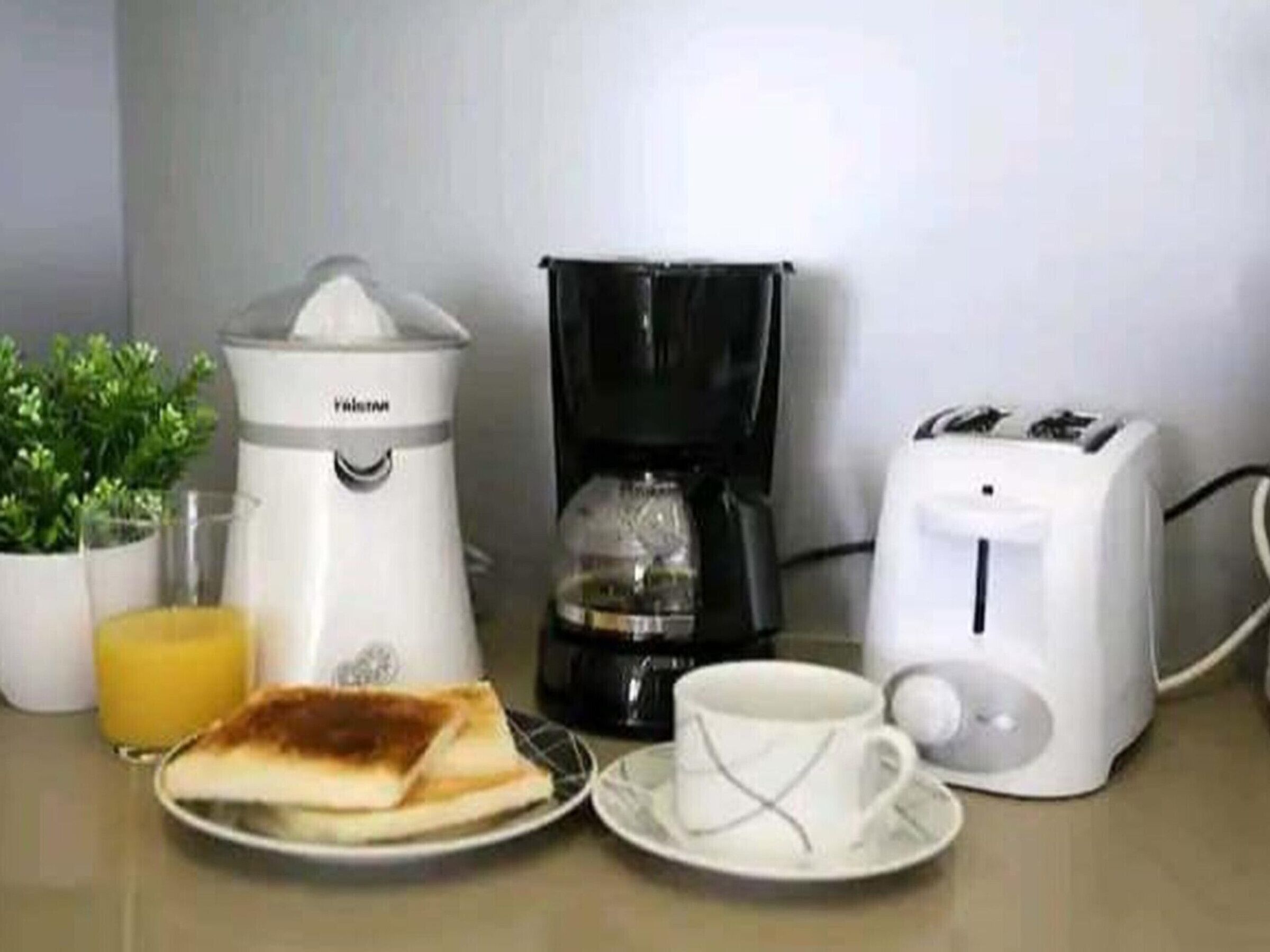 A breakfast setup with a coffee maker, toaster, cup, and a plate with toast.