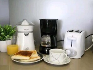 Mesa de café da manhã com cafeteira, torradeira, xícara e um prato com torradas.