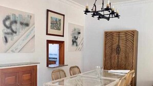 Un coin repas avec une table en verre, des chaises en osier et des œuvres d’art accrochées aux murs.
