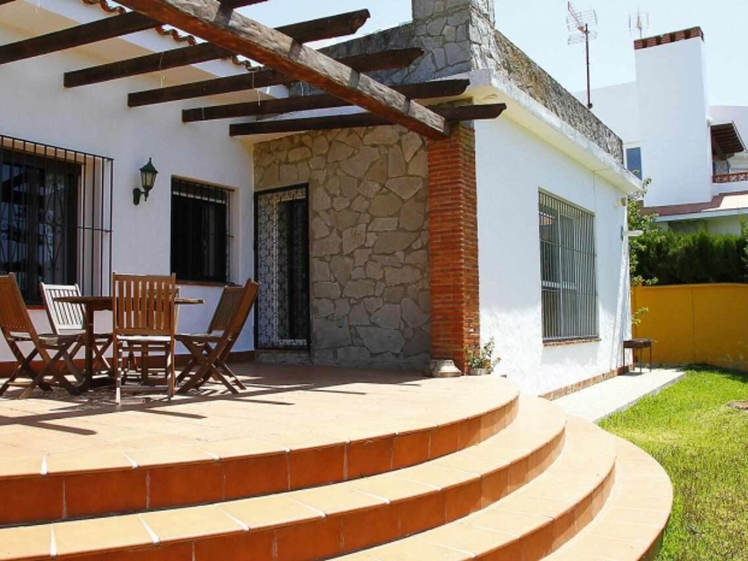 Un patio cubierto con un muro de piedra, una mesa de madera con sillas y un conjunto de escalones que conducen a una puerta.