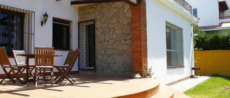 Un patio cubierto con un muro de piedra, una mesa de madera con sillas y un conjunto de escalones que conducen a una puerta.