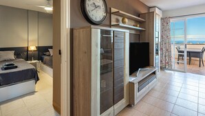 A modern living room with a large flat-screen TV, a wooden cabinet, and a glass door leading to a balcony with a view. - Penthouse in Los Cristianos with Large Pools (Los Cristianos)