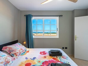 Un dormitorio con cama, ventana con vistas, puerta y ventilador de techo.