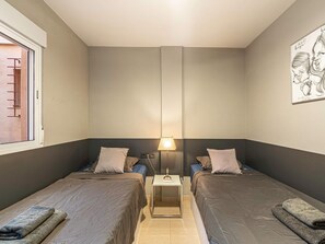 A room with two beds, a nightstand with a lamp, a window with a view, and a wall with a framed picture. - Penthouse in Los Cristianos with Large Pools (Los Cristianos)