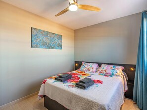 A bedroom with a bed, a ceiling fan, a wall-mounted painting, and a nightstand.