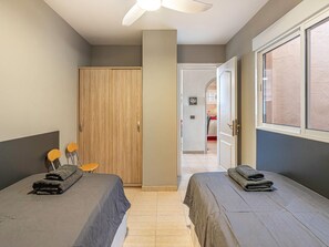 A bedroom with two beds, a wooden wardrobe, a ceiling fan, and a view through an open door to a bathroom. - Penthouse in Los Cristianos with Large Pools (Los Cristianos)