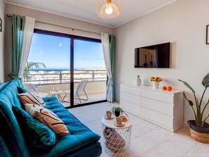 A modern living room with a teal sofa, a small round table, and a white cabinet.