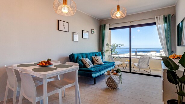Un salon moderne avec une table à manger, un canapé bleu et un balcon offrant une vue sur la mer.