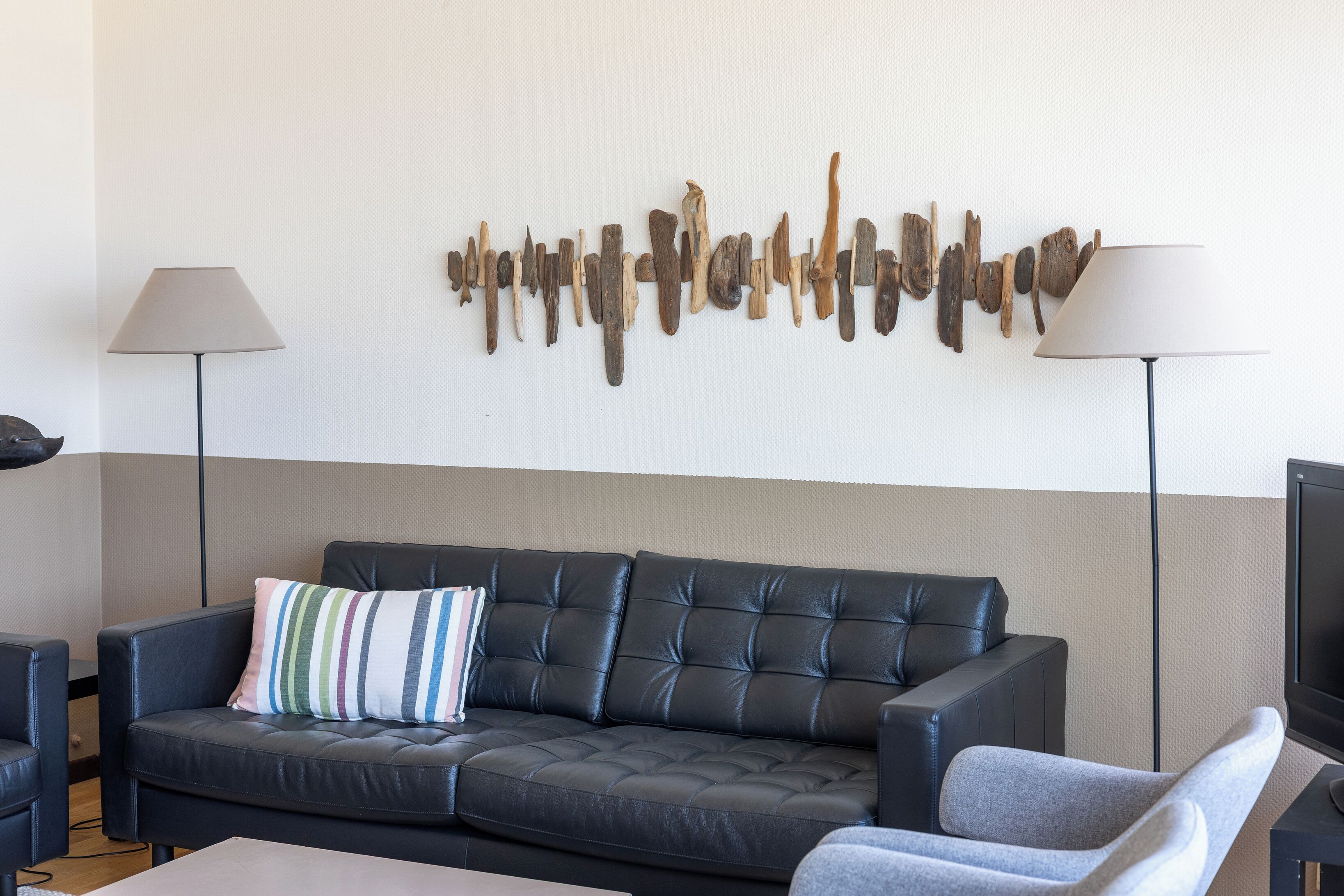 A modern living room with a sectional sofa, a striped pillow, two floor lamps, and a wall art piece.