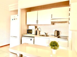 A modern kitchen with white cabinets, a microwave, a kettle, and a sink.