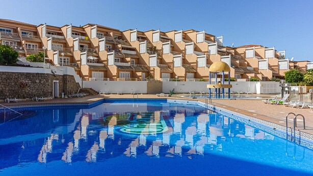 En swimmingpool som speglar byggnaderna, omgiven av en stenmur och en klar himmel.