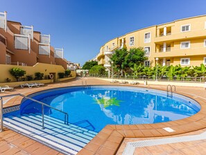 A swimming pool with steps leading into it, surrounded by a tiled deck and a building with balconies.