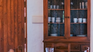 A dining table with chairs, a wooden cabinet with glass doors, and a wall-mounted light switch.