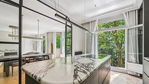 Une cuisine moderne dotée d’un plan de travail en marbre, de grandes fenêtres et d’un coin repas avec une table et des chaises.
