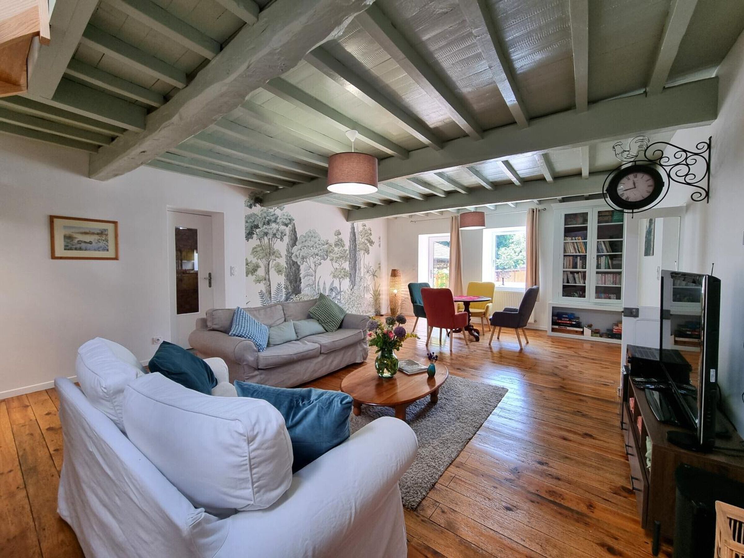 A spacious living room with a high ceiling, a fireplace, a dining area with chairs, and a bookshelf.