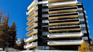 En hög byggnad med flera våningar och balkonger, troligen ett hotell eller ett bostadskomplex, omgiven av träd och snö.