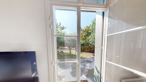 A room with a Samsung TV on a wooden stand, a sliding glass door leading to an outdoor area with a bench and trees. - House in Vic-la-Gardiole, 2 pers, Terrace, Close to Beach (Vic-la-Gardiole)