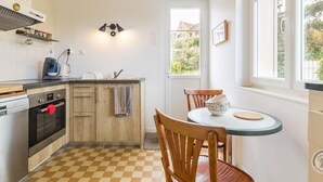 A compact kitchen with a checkered floor, wooden cabinets, a built-in oven, a coffee maker, and a window with a view of greenery. - House in St Pair-sur-Mer with Garden and Private Parking, Near the Beach (Saint-Pair-sur-Mer)