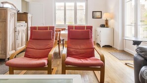 A room with two red chairs, a wooden cabinet, a table, and a window with a view of a fence. - House in St Pair-sur-Mer with Garden and Private Parking, Near the Beach (Saint-Pair-sur-Mer)