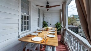 A covered porch with a wooden table set for dining, white walls, and a view of the neighborhood.