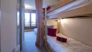 Quarto com beliche, escada de madeira, janela com cortinas e vista para o exterior.