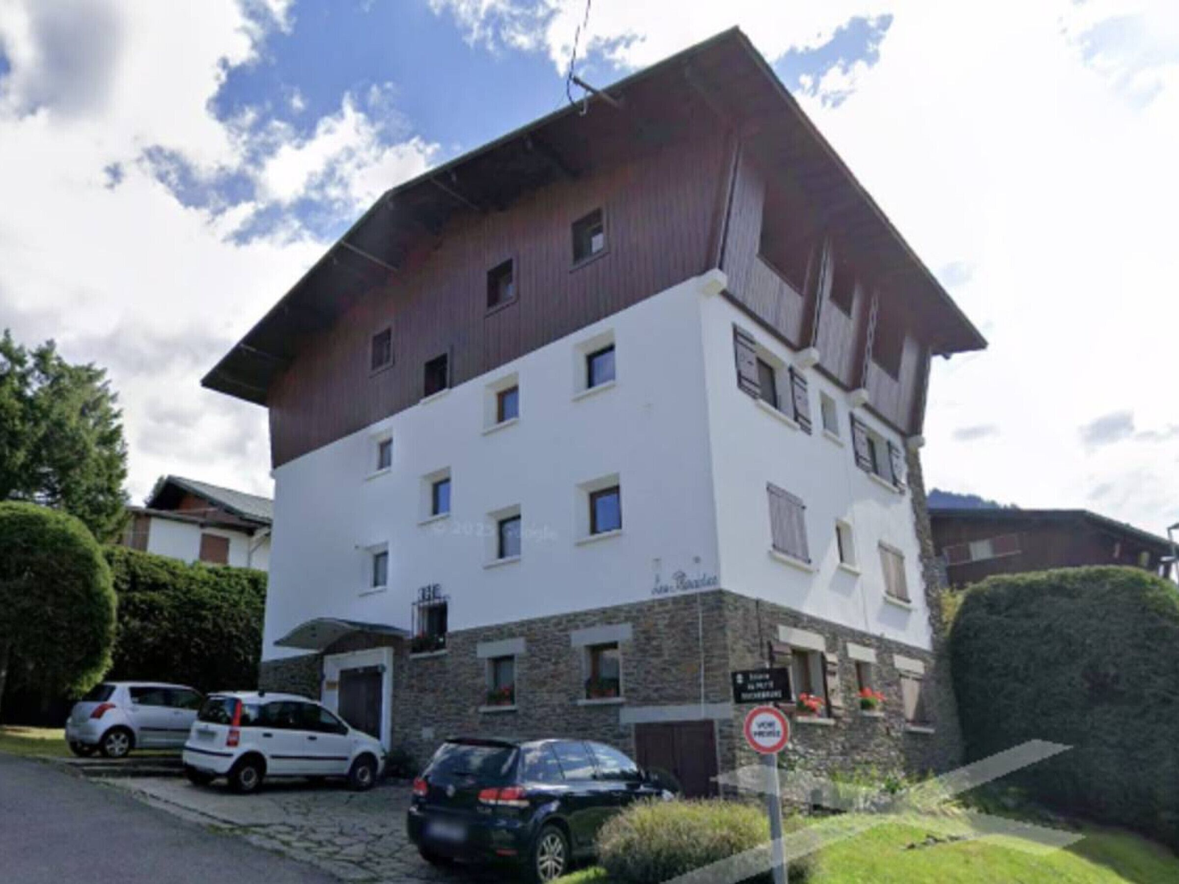 A multi-story building with a white facade and brown roof, featuring several windows and a sign indicating a no parking zone.