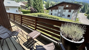 Une terrasse en bois avec deux chaises et un pot de fleurs, donnant sur un paysage montagneux parsemé de maisons.