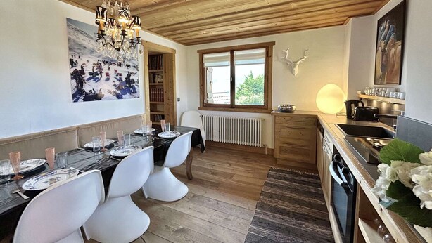 Un espace repas doté d’un plafond en bois, d’un lustre, d’un grand tableau, d’une fenêtre offrant une vue agréable et d’une cuisine équipée d’un  évier et d’une cuisinière.