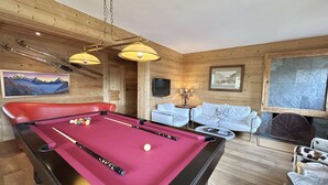 Une table de billard avec des billes, un canapé rouge, un canapé blanc et une cheminée.