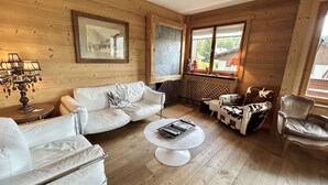 Un salon chaleureux avec un canapé blanc, une table basse et un fauteuil à motifs de vaches. On y trouve une cheminée, une fenêtre avec vue et une lampe sur une table d’appoint.