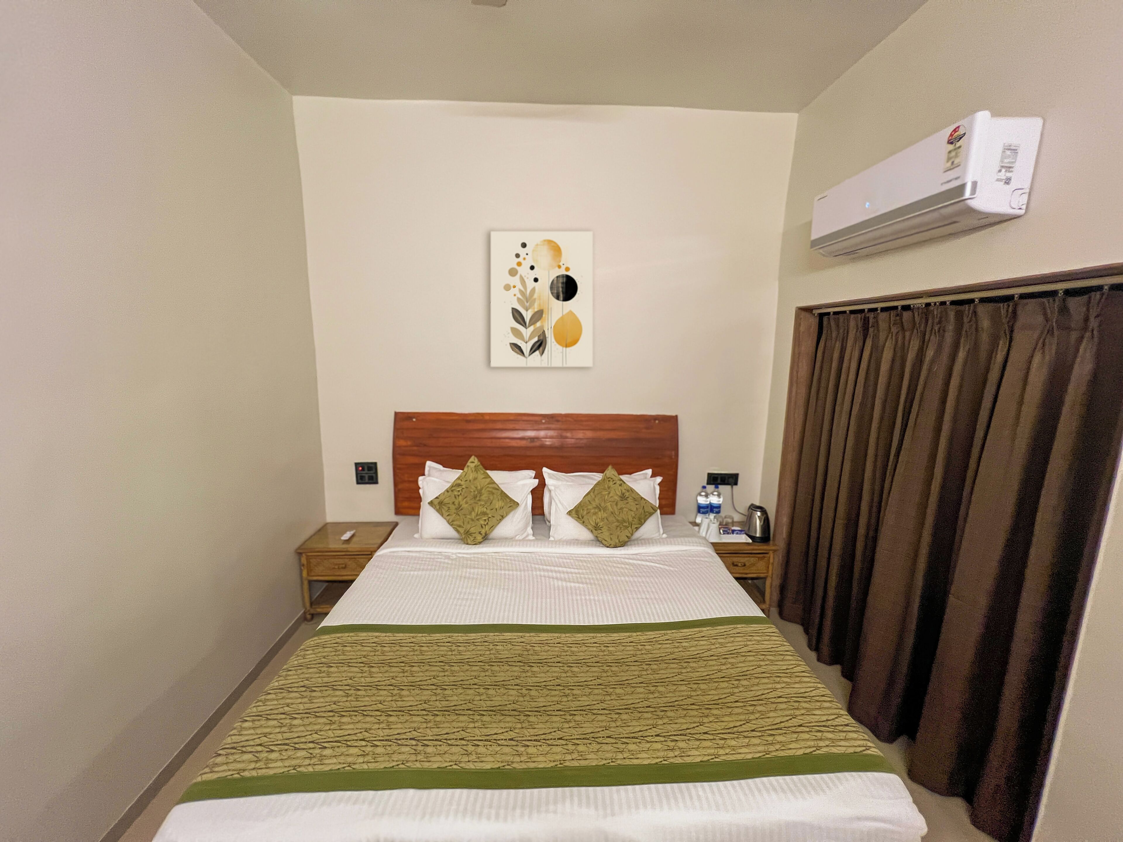 A hotel room with a bed, a nightstand, an air conditioner, and a curtain.