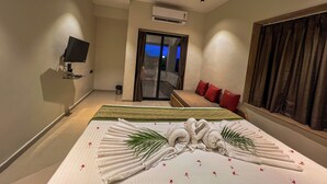 Quarto de hotel com cama, televisão, ventoinha no teto e vista para o exterior.