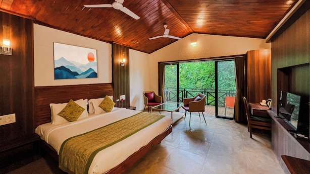 Um quarto espaçoso com uma cama grande, uma mesa de vidro e cadeiras, uma varanda com televisão e um ventilador de teto.