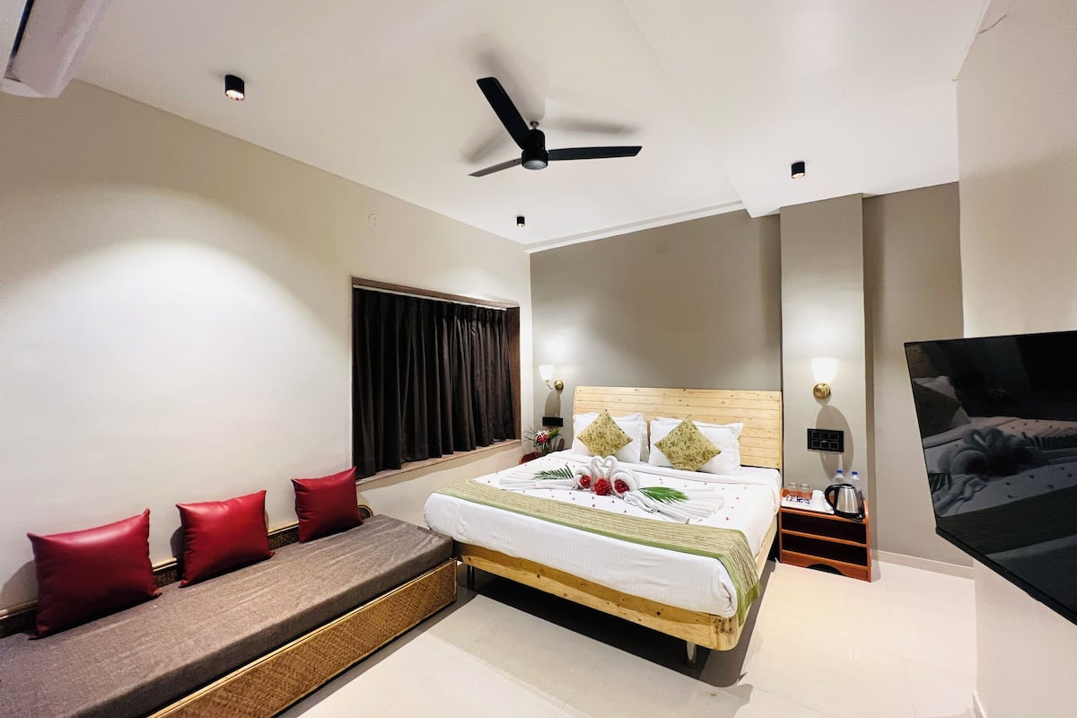 A modern hotel room with a bed, a sofa, a ceiling fan, and a TV.