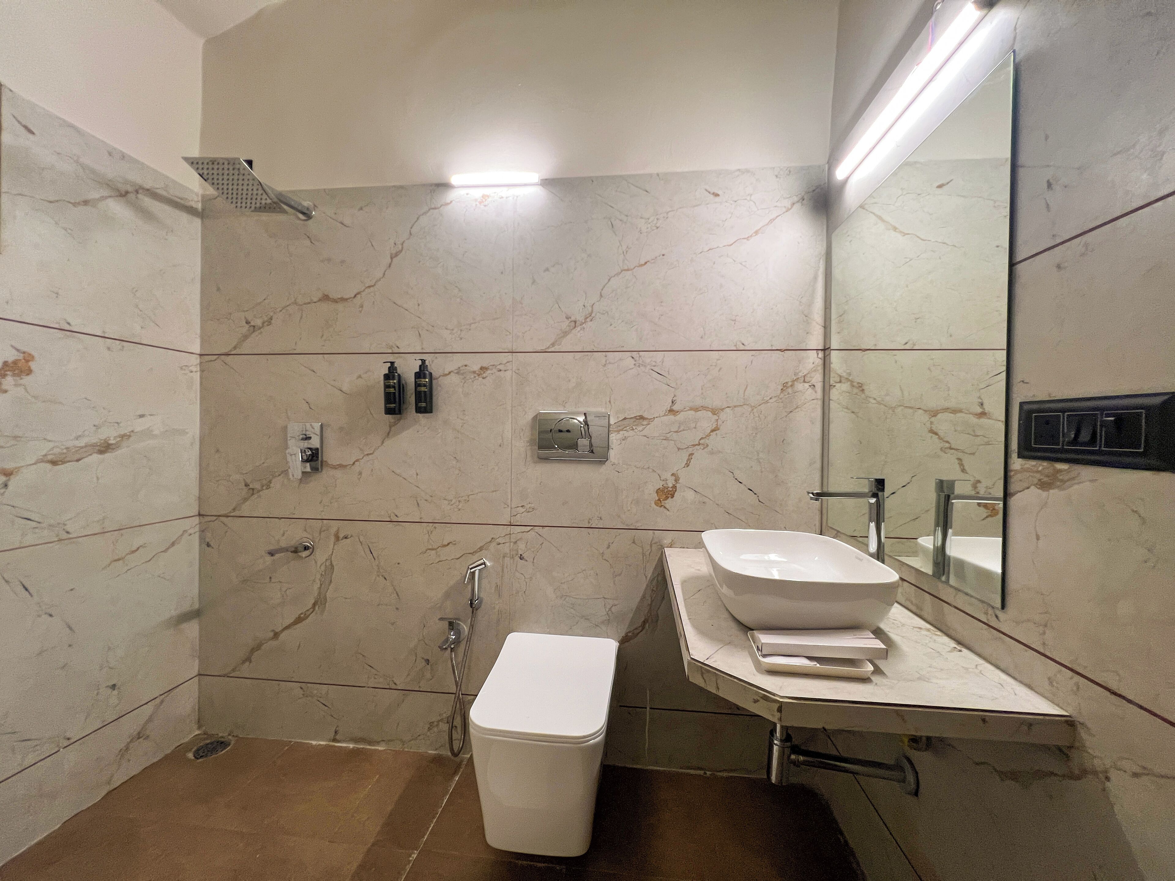 Un baño moderno con pared de mármol, lavamanos blanco, inodoro y zona de ducha.