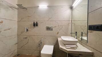 Un baño moderno con pared de mármol, lavamanos blanco, inodoro y zona de ducha.