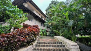 Um edifício com estilo arquitetônico tradicional, rodeado por vegetação exuberante e uma escadaria de pedra que leva à entrada.