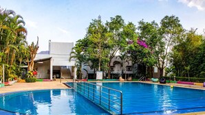 Piscina com grade de metal, cercada por árvores e um edifício com telhado plano.