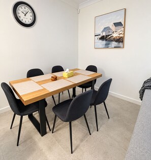 A dining area with a wooden table, black chairs, a clock on the wall, and a framed picture.