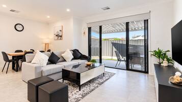 A modern living room with a sofa, coffee table, and a dining area with chairs and a table.