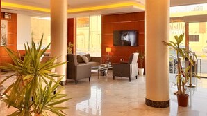 A lobby with a seating area, a flat-screen TV mounted on the wall, and large pillars.