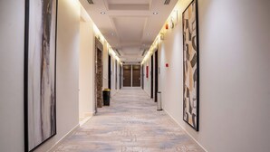 A hotel hallway with a patterned floor, framed artwork on the walls, and doors leading to rooms.