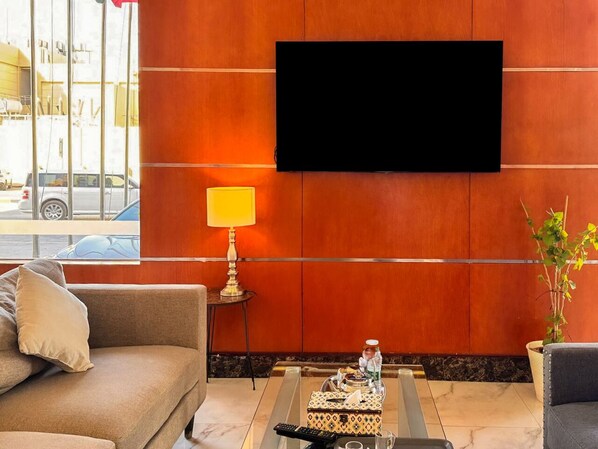 A hotel lobby with a sofa, a coffee table, a lamp, a television, and a potted plant.