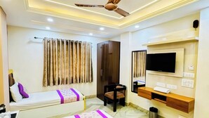 A hotel room with a large bed, a smaller bed, a TV, a ceiling fan, and a bathroom with a shower.