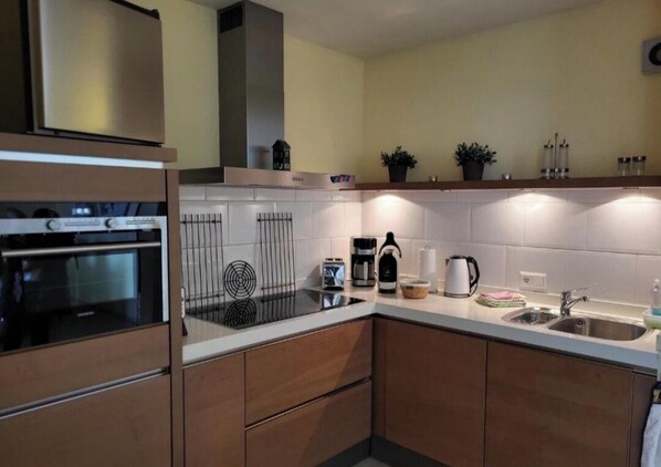 A modern kitchen with a built-in oven, a coffee maker, and a kettle on the countertop.