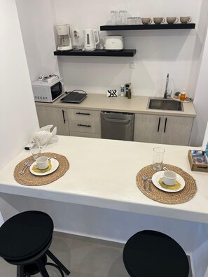 A compact kitchen with a white countertop, two black stools, a fish-shaped salt shaker, and a coffee machine.