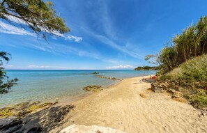 A beach with clear turquoise water, sandy shore, and some vegetation.